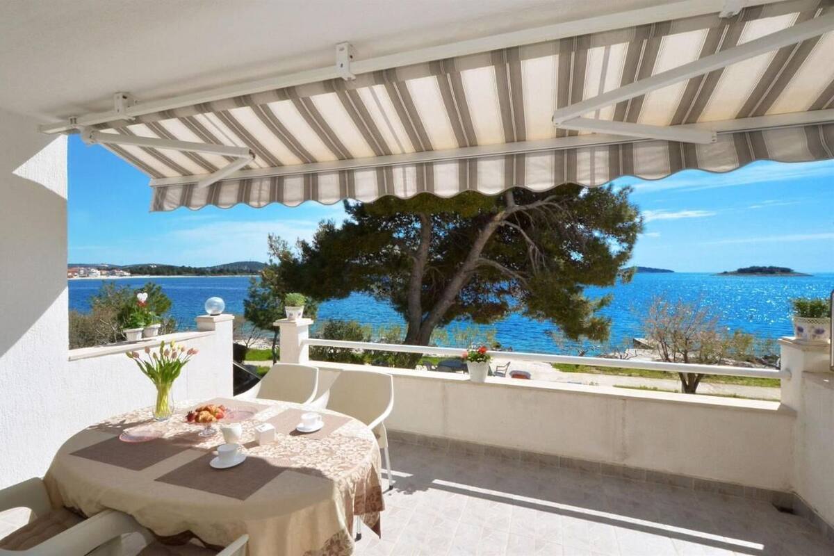 Un balcon avec une table dressée pour deux personnes, donnant sur une étendue d’eau et un arbre.