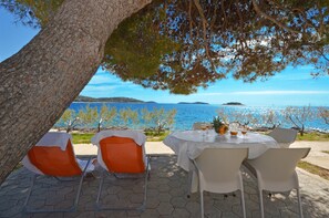 An outdoor dining area with a table set for two, overlooking a body of water with distant landforms. - Apartments Nina (Rogoznica)
