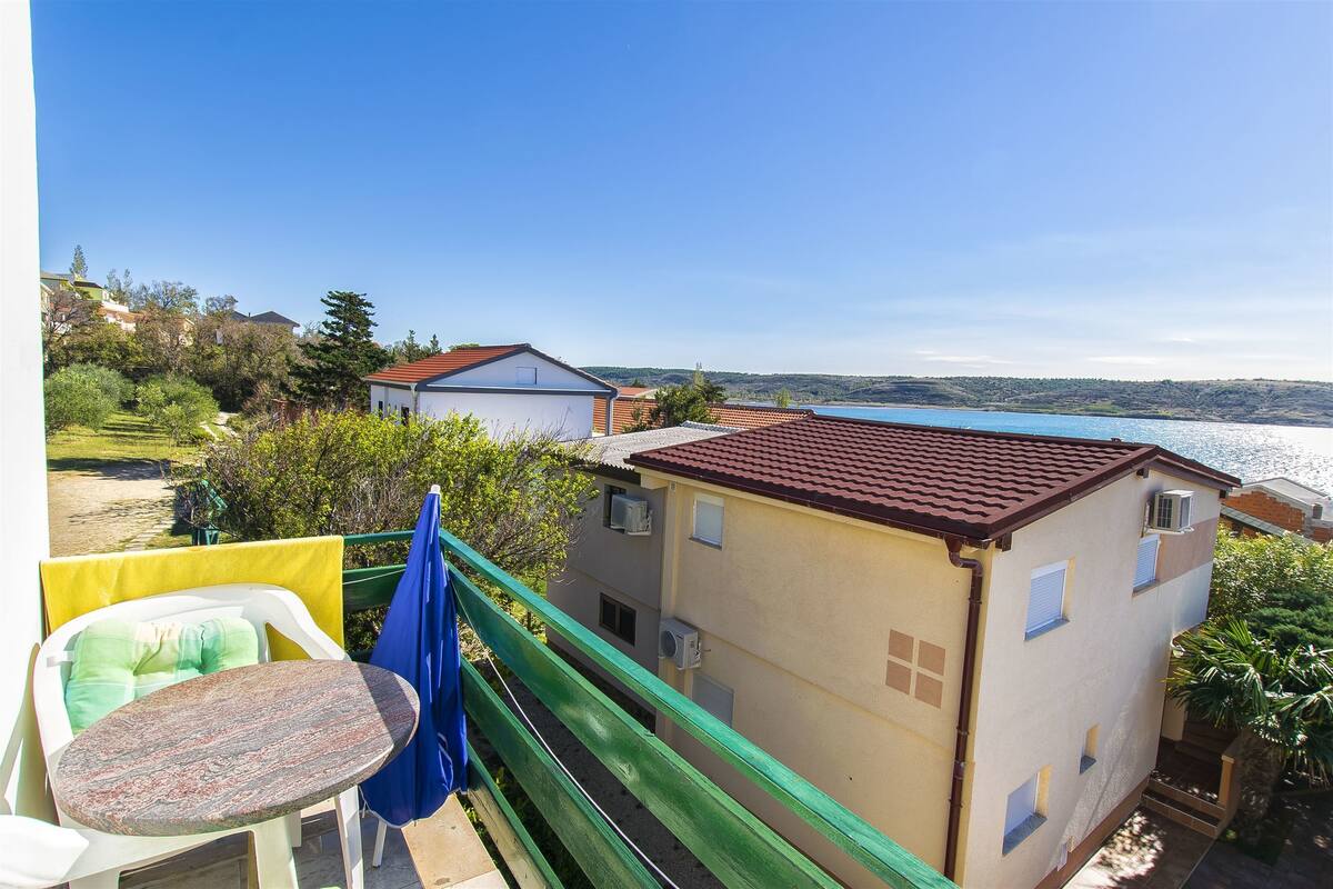 A balcony with a table and chairs, overlooking a body of water and a hillside.