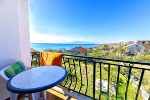 A balcony with a round table and chairs, overlooking a coastal landscape with houses and greenery. - Apartments Milena (Rtina)