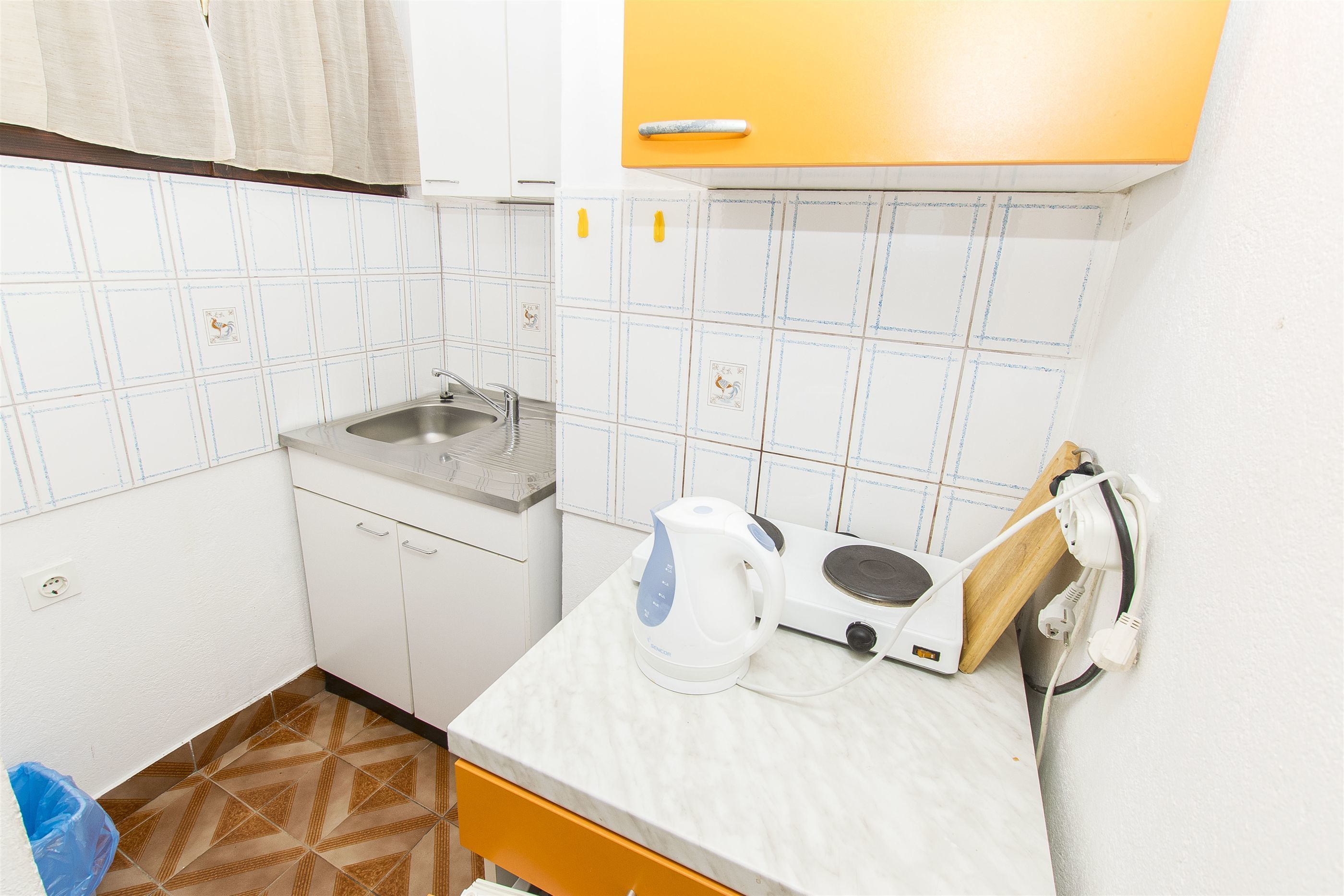 A small kitchen with white cabinets, a sink, a kettle, and a toaster on the counter.