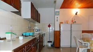 A kitchen with wooden cabinets, a stove, a sink, and a refrigerator. There is a broom leaning against the wall and a table with chairs in the corner. - House Fani (Zastrazisce)