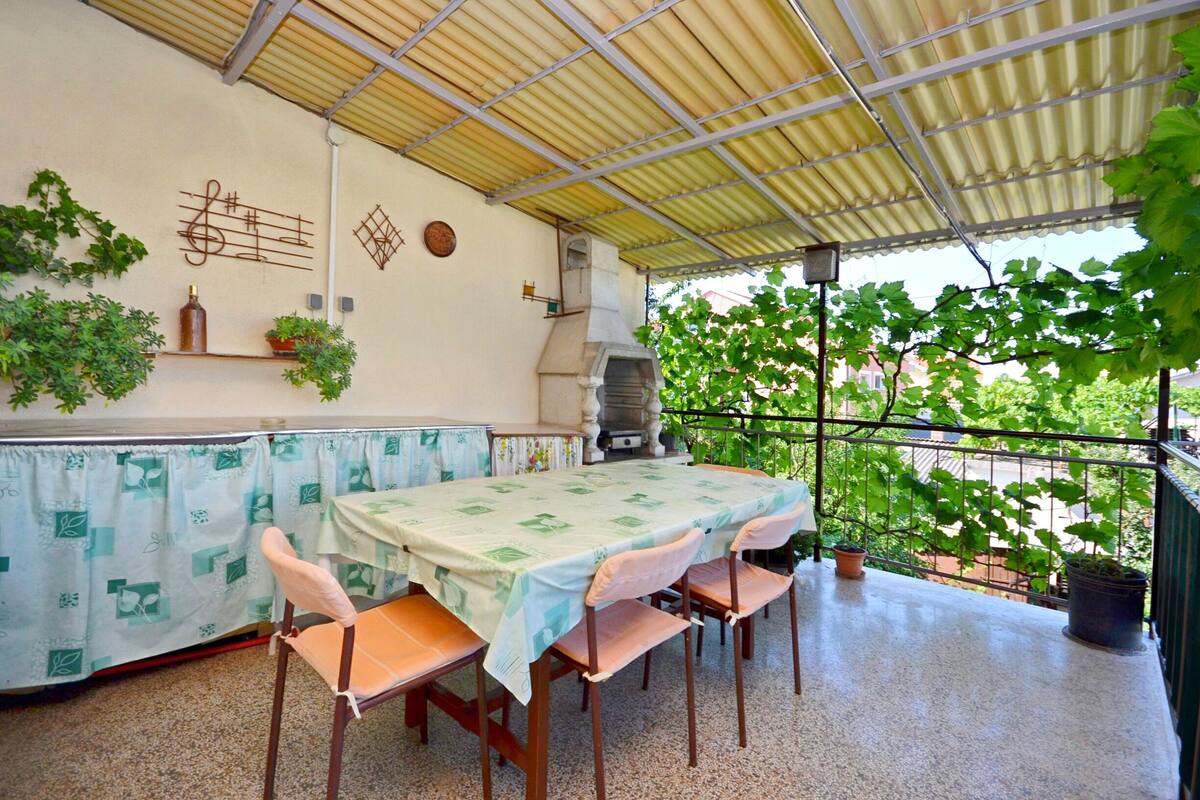 Une terrasse extérieure avec une table et des chaises, un barbecue, des plantes en pot et une vue sur la verdure.