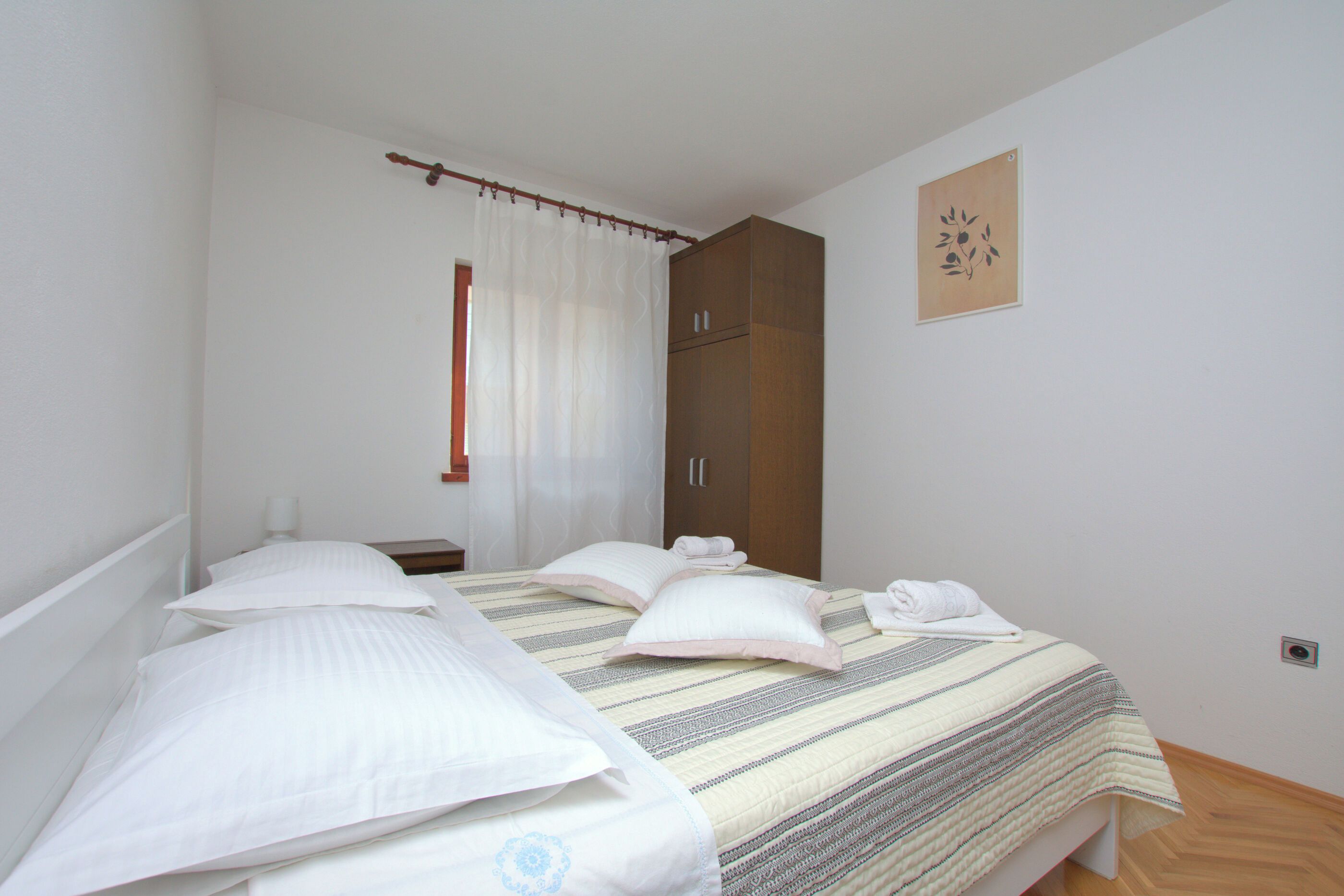 A bedroom with a bed, pillows, a nightstand, a wardrobe, and a window with curtains.