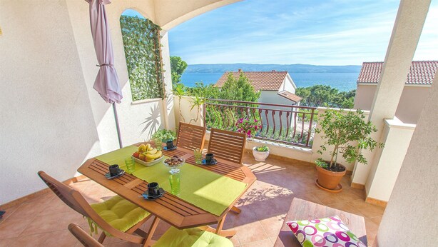A balcony with a table set for two, a potted plant, and a view of the sea. - Apartment Jordan (Duce)