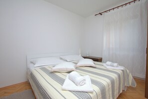 A neatly made bed with pillows and a rolled towel, a bedside table with a lamp, and a window with sheer curtains. - Apartment Jordan (Duce)