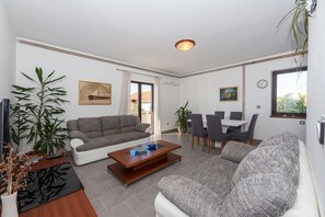 A modern living room with a sofa, coffee table, and dining area. - Apartments Snjezana (Tisno)
