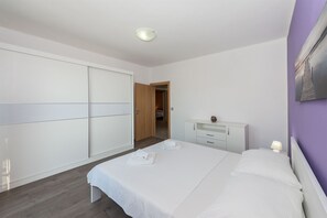 A bedroom with a bed, a nightstand, a dresser, a wardrobe, and a door leading to another room. - Apartments Snjezana (Tisno)