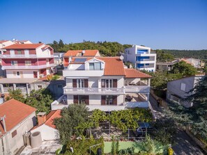 A multi-story residential building with balconies, solar panels, and a green area with trees and a car. - Apartments Snjezana (Tisno)