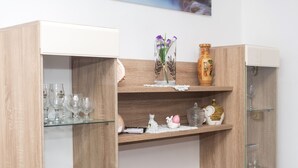 Un mueble de madera con estantes que contiene cristalería, un jarrón con flores y objetos decorativos.