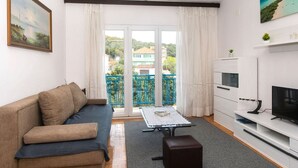 Una sala de estar con sofá, mesa de centro, televisor y un balcón con vistas a edificios.