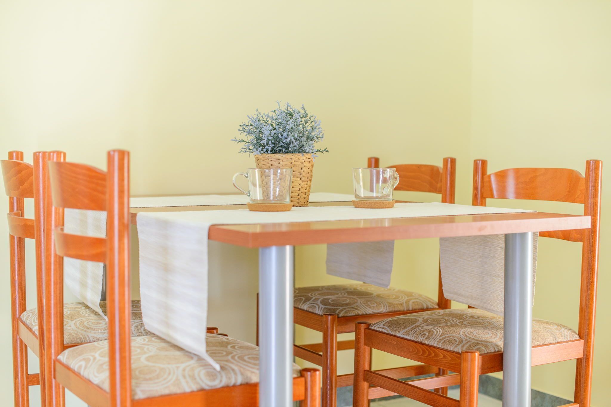 A dining table with a woven plant centerpiece, surrounded by wooden chairs with cushioned seats.