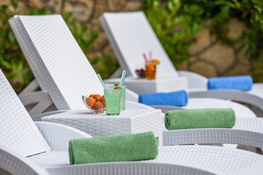 Zona de piscina con sillones de descanso y una mesa con bebidas y frutas.