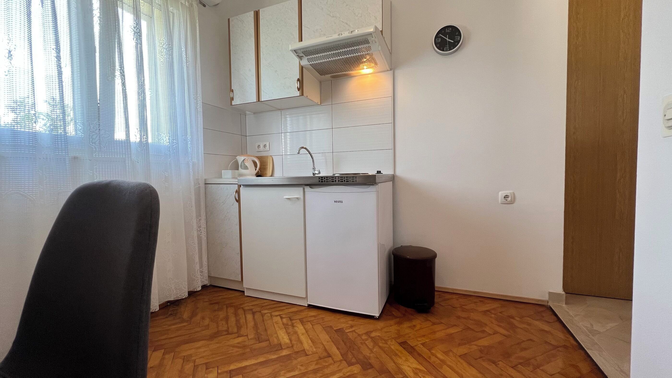A compact kitchen with a sink, a kettle, and a clock on the wall.