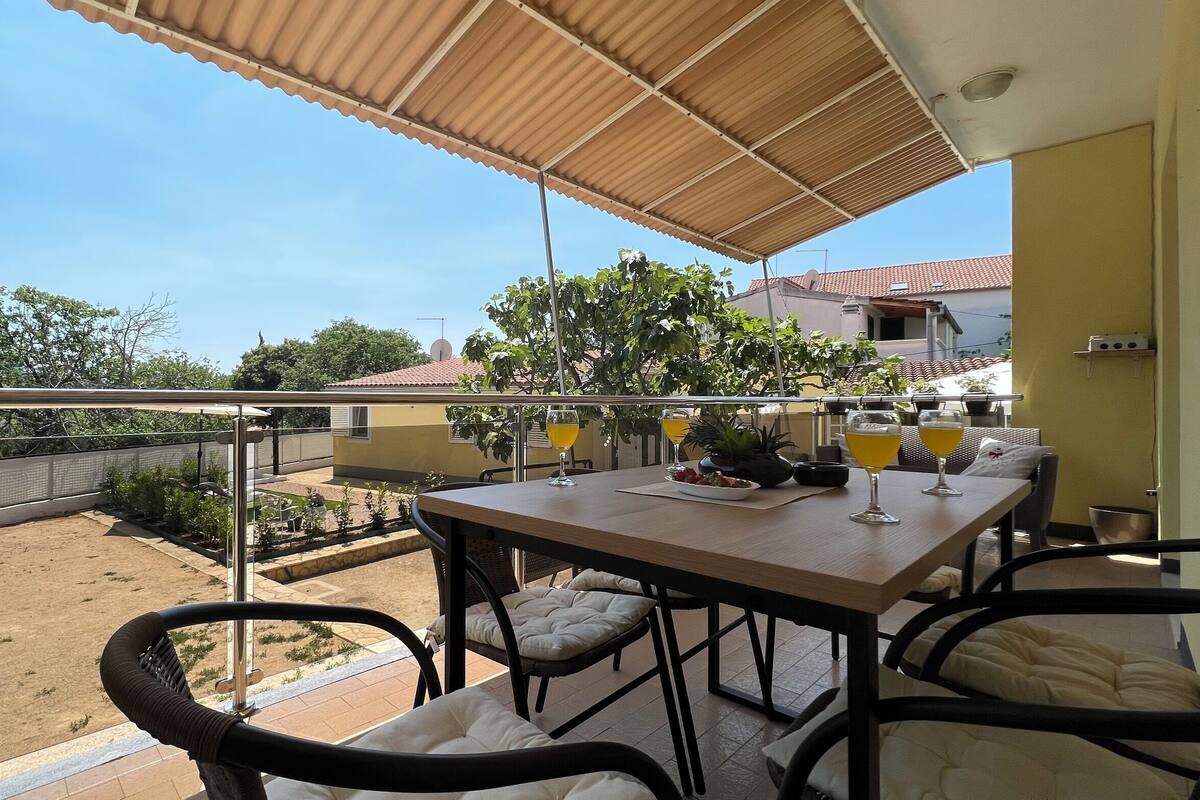 A balcony with a table set for two, two glasses of orange juice, a bowl of strawberries, and a potted plant.