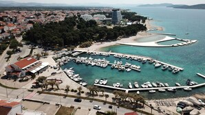 Vista aérea de un puerto deportivo costero con barcos amarrados, rodeado de edificios residenciales y un cielo despejado.