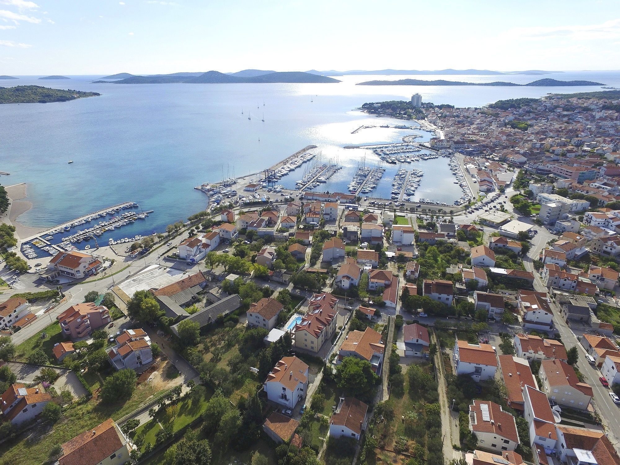 Vista aérea de un pueblo costero con un puerto deportivo, edificios residenciales y una vista despejada del mar.
