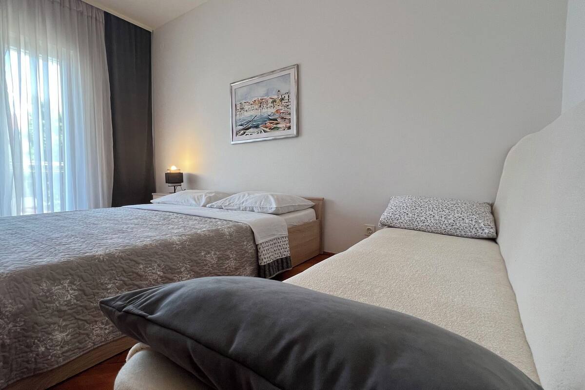 A hotel room with a bed, a sofa, a nightstand with a lamp, and a painting on the wall.