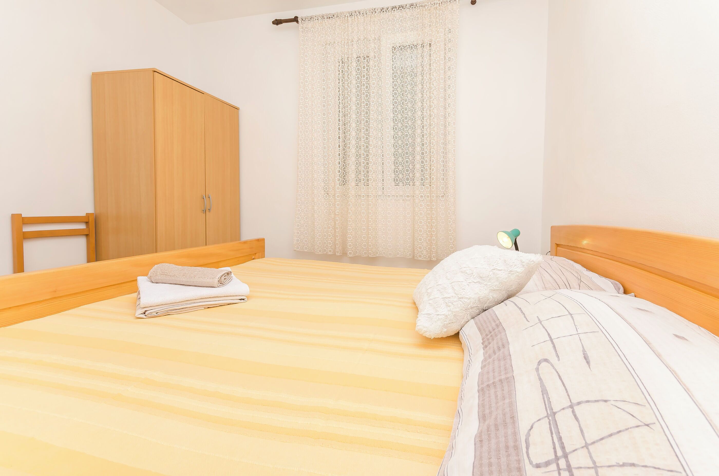 Une chambre à coucher avec un lit, une armoire en bois et une fenêtre ornée de rideaux en dentelle.