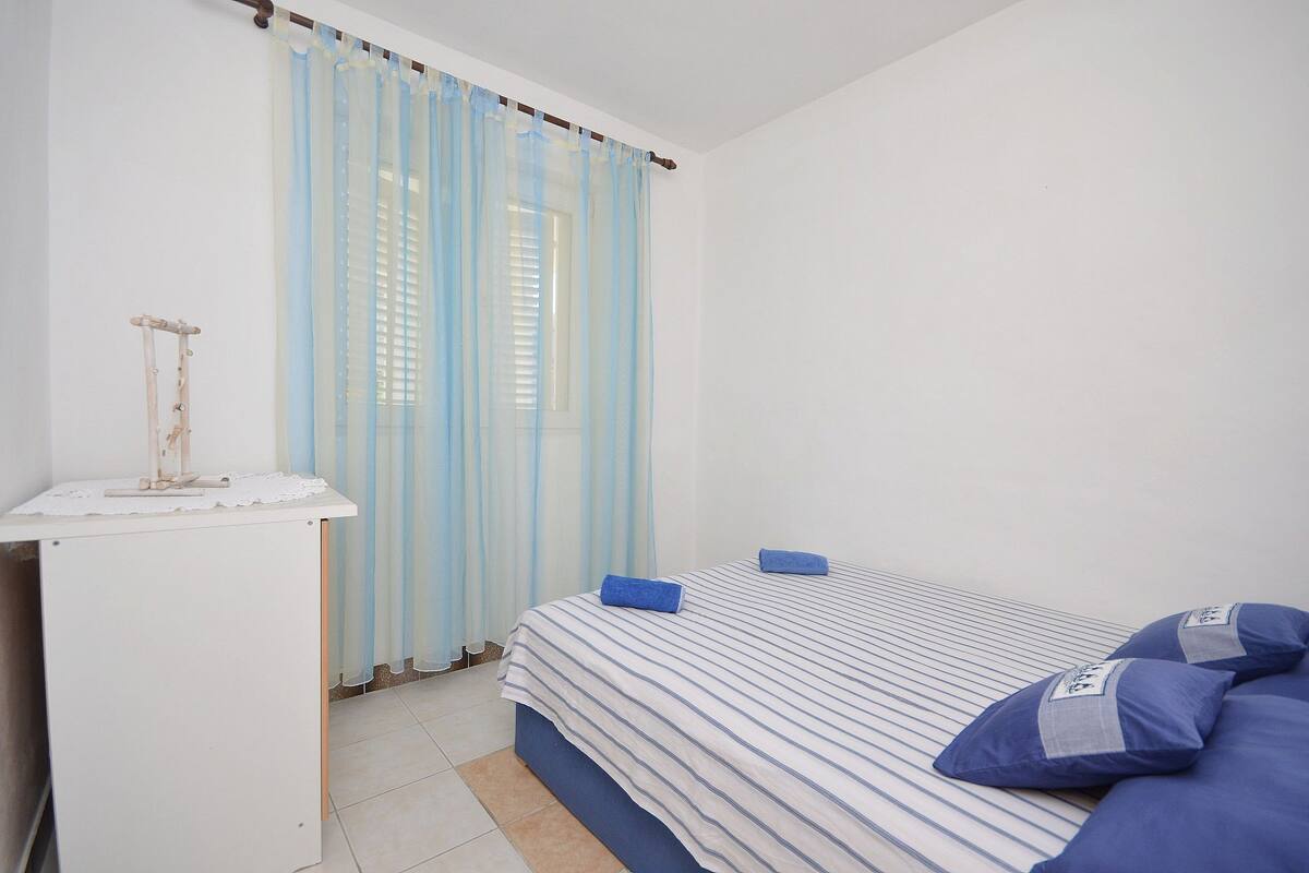 A bedroom with a bed, a nightstand, and a window with curtains.