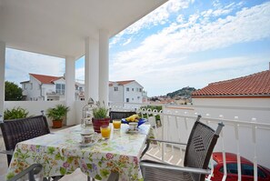 A balcony with a table set for breakfast, potted plants, and a red car parked nearby. - Apartments Mila Family With Pool (Tribunj)