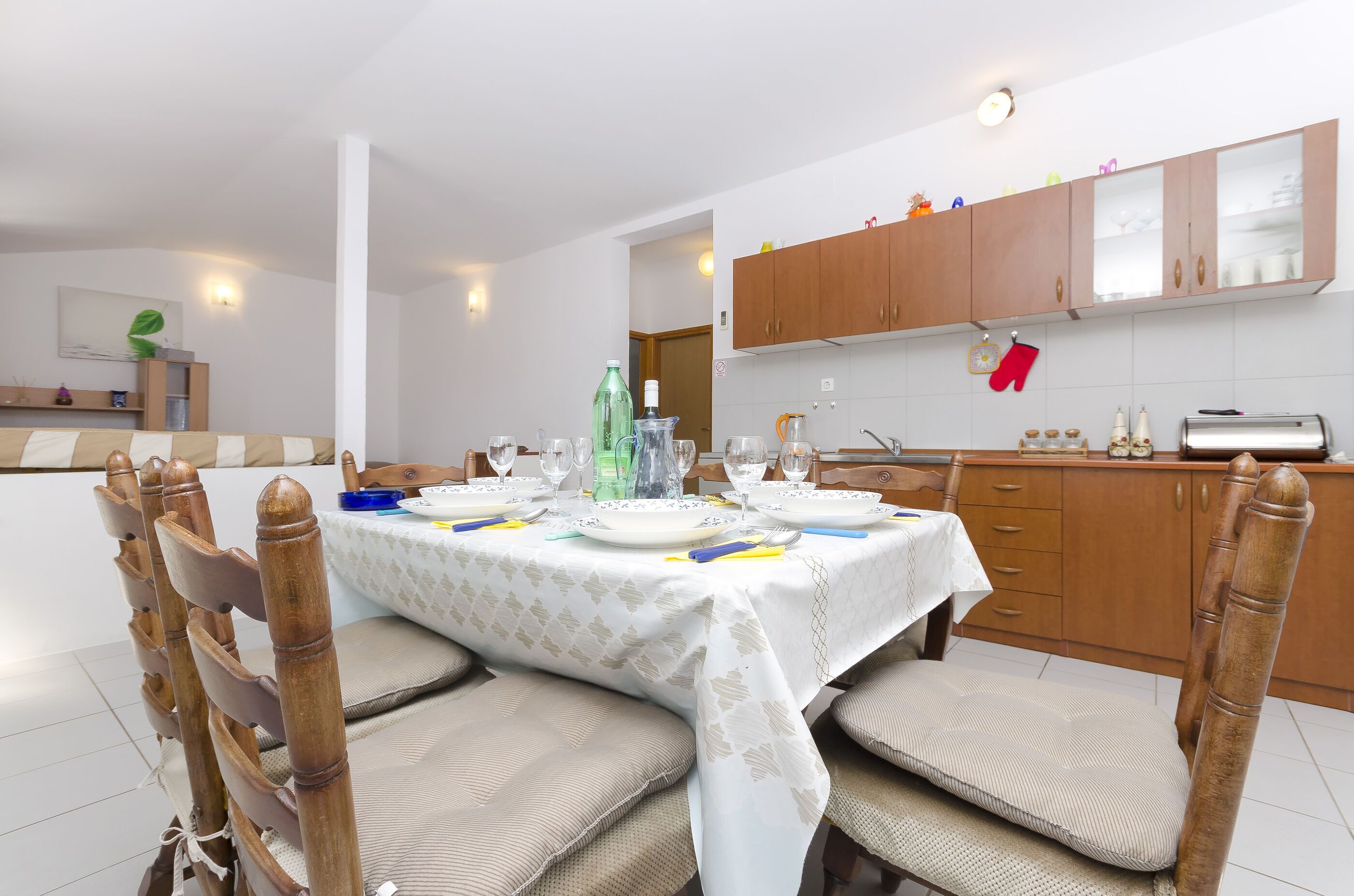 Un comedor con una mesa dispuesta para cuatro personas, sillas de madera y una cocina al fondo.