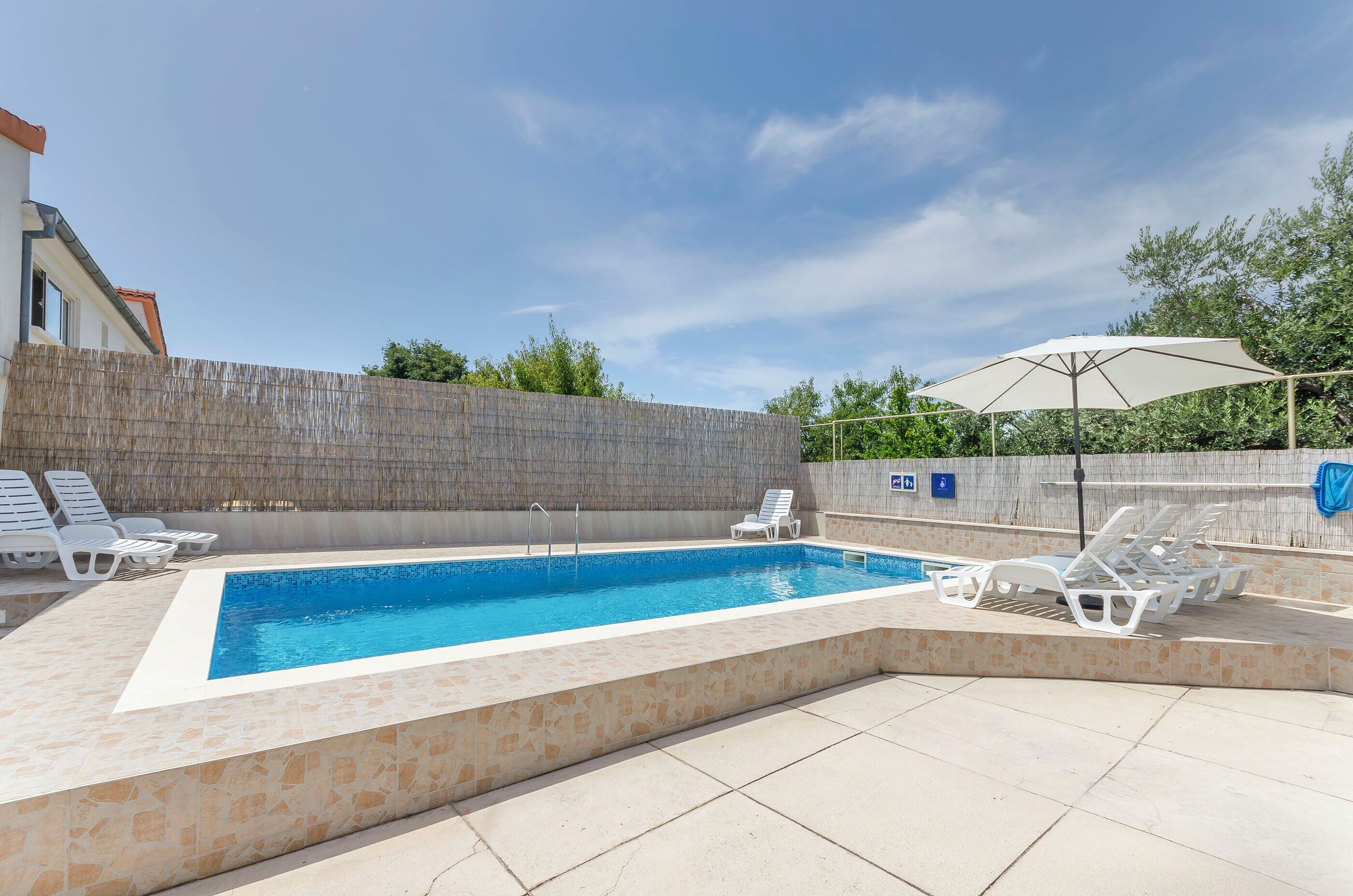 A rectangular swimming pool with a tiled edge, surrounded by lounge chairs and a covered umbrella.
