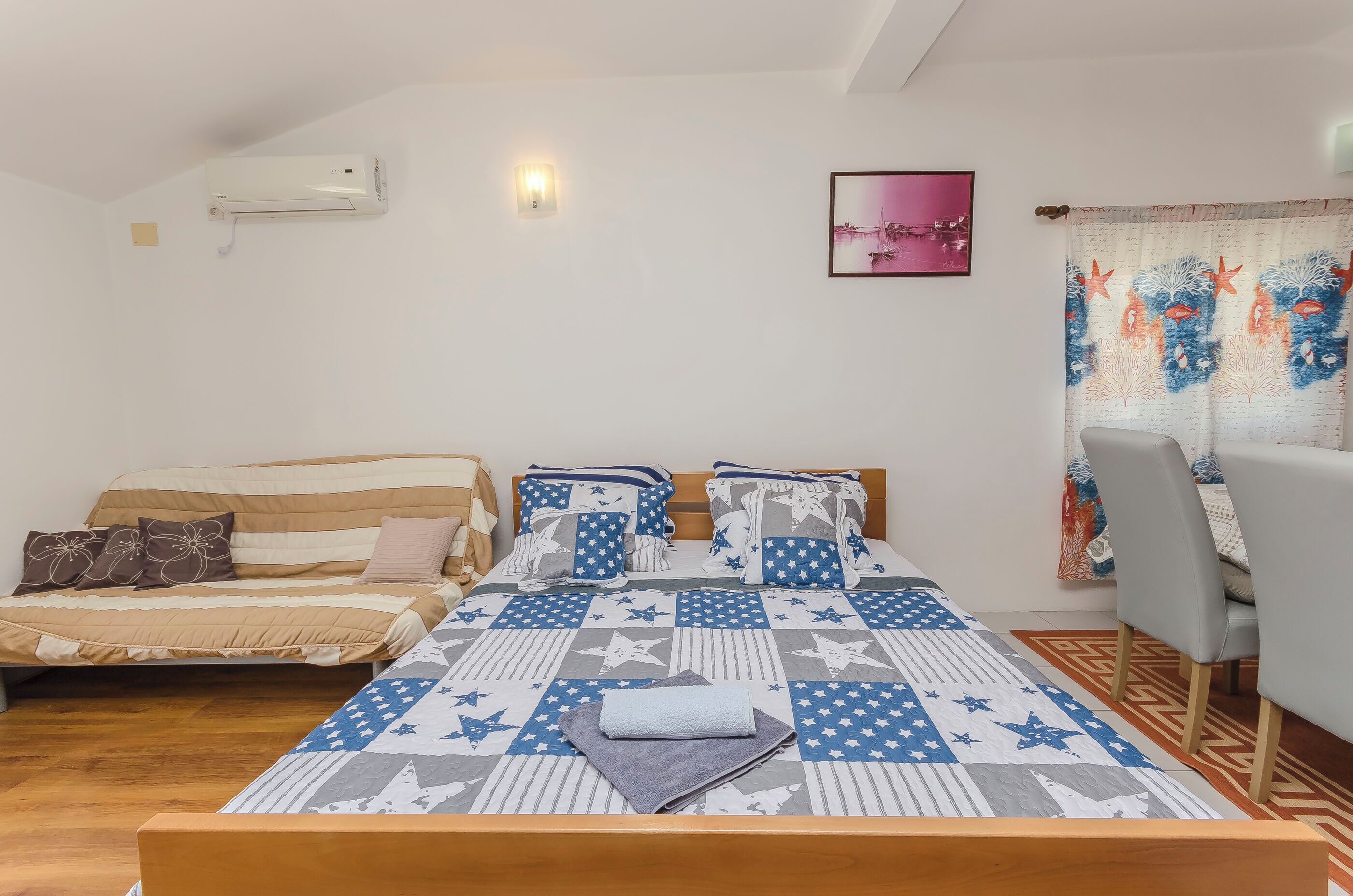 A bedroom with two beds, a dining area, and a window with patterned curtains.