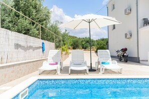 A swimming pool with three white lounge chairs and a large umbrella. - Apartments Mila Family With Pool (Tribunj)