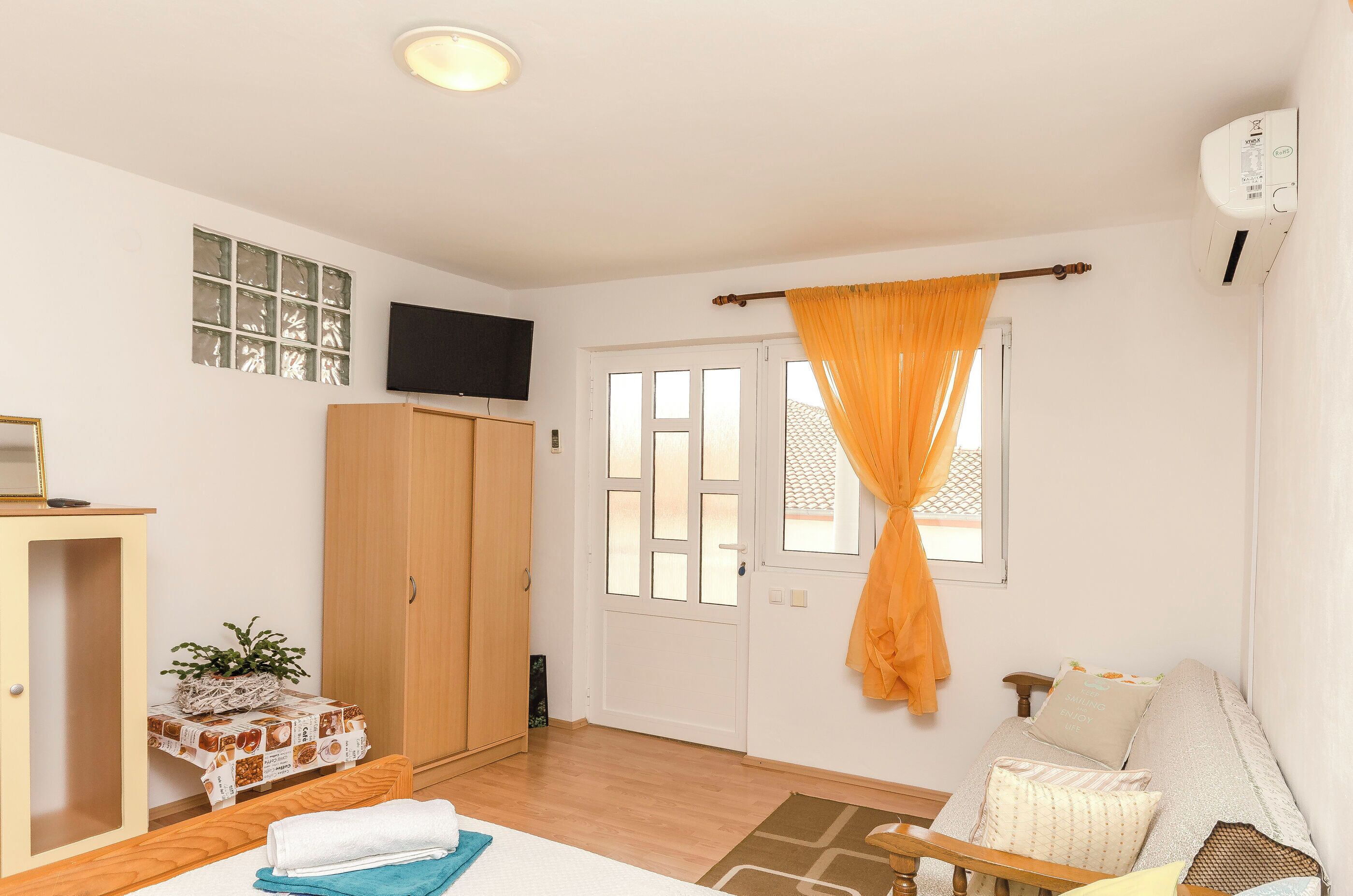 Ein Zimmer mit einem Bett, einem Kleiderschrank, einem an der Wand montierten Fernseher und einem Fenster mit Vorhängen.