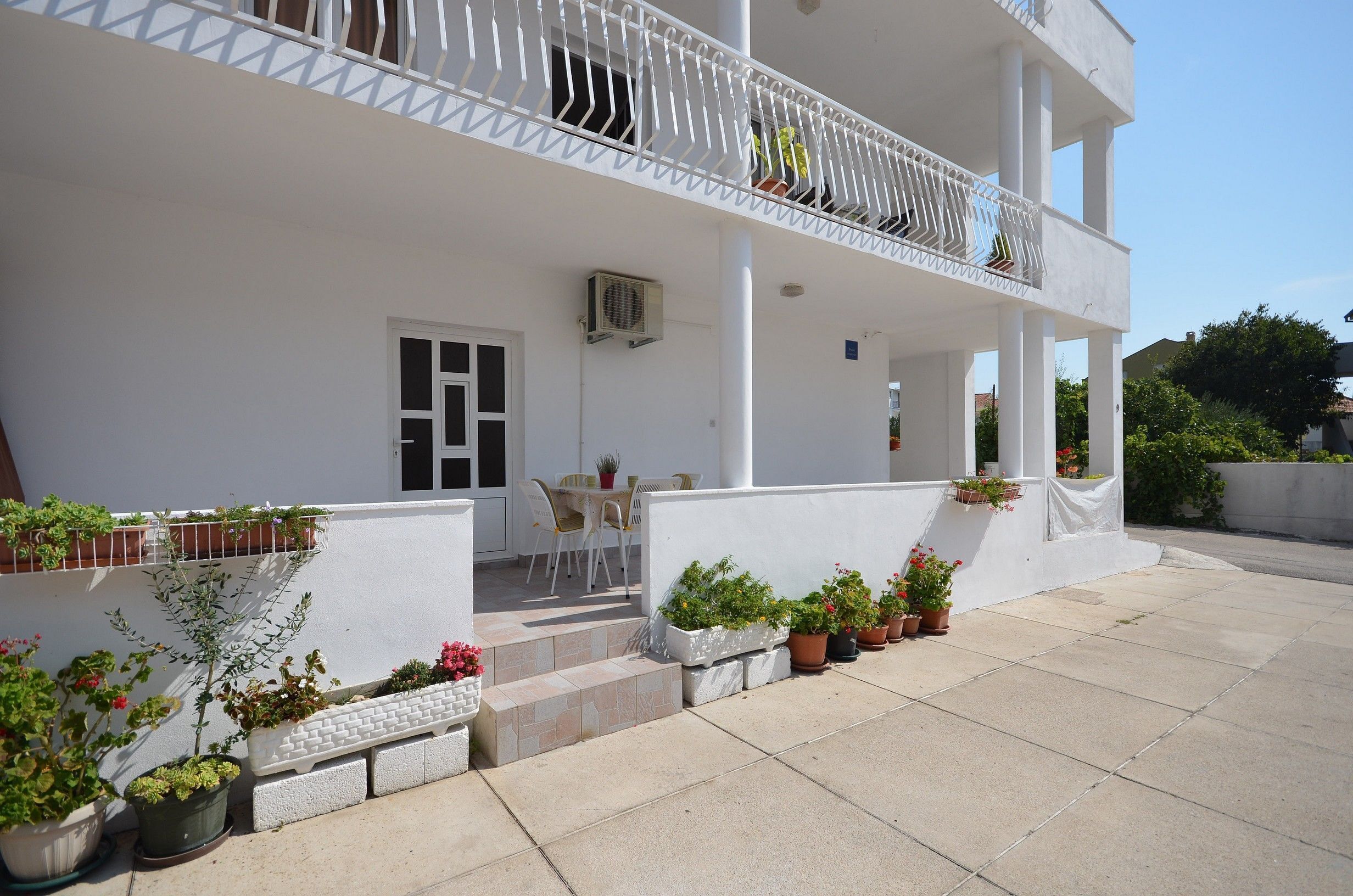 Ein weißes Gebäude mit Balkon, Blumentöpfen und einem Tisch mit Stühlen.