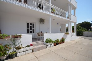 A white building with a balcony, potted plants, and a table with chairs. - Apartments Mila Family With Pool (Tribunj)