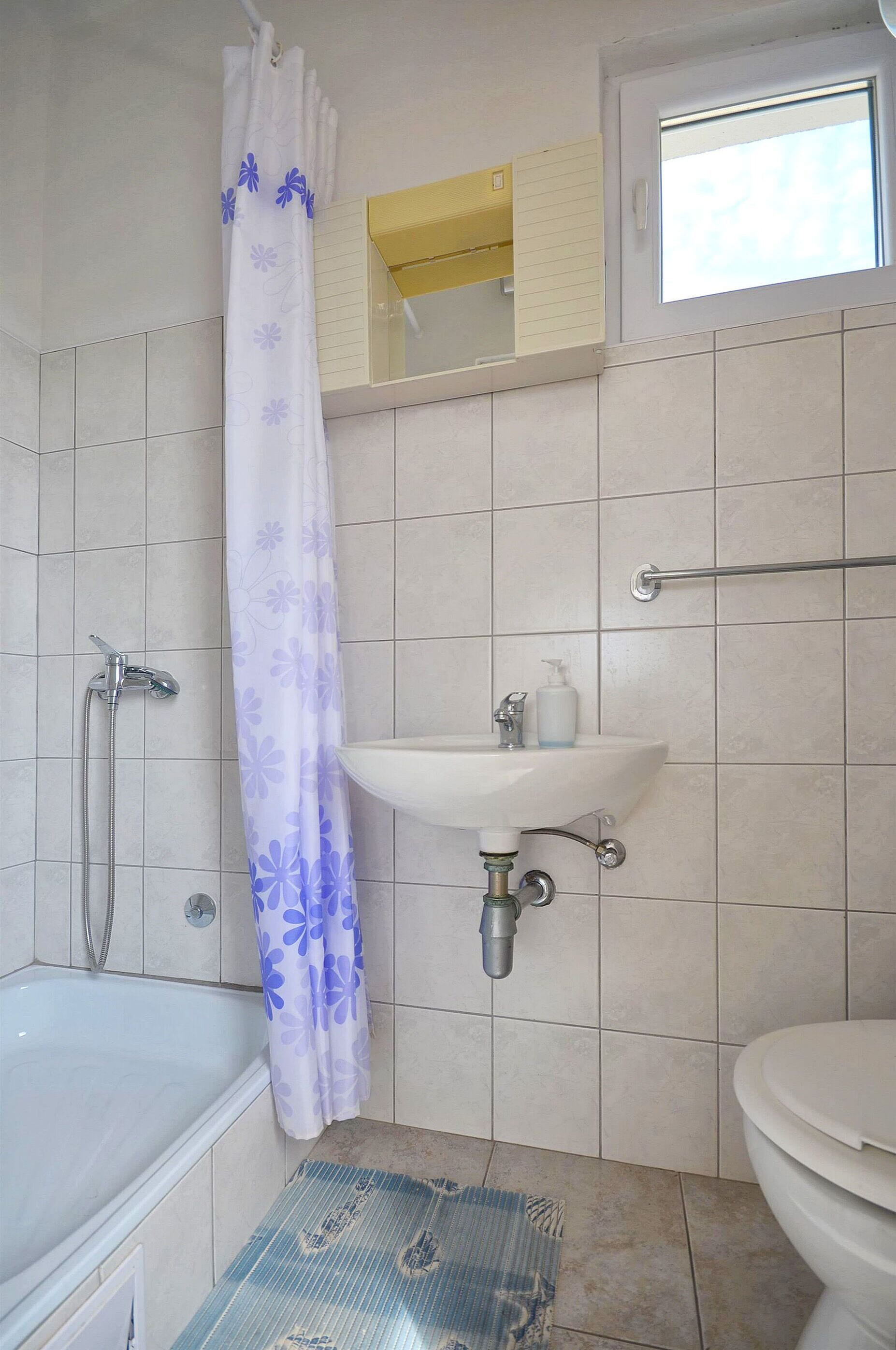 A bathroom with a shower, a sink, a toilet, and a window.