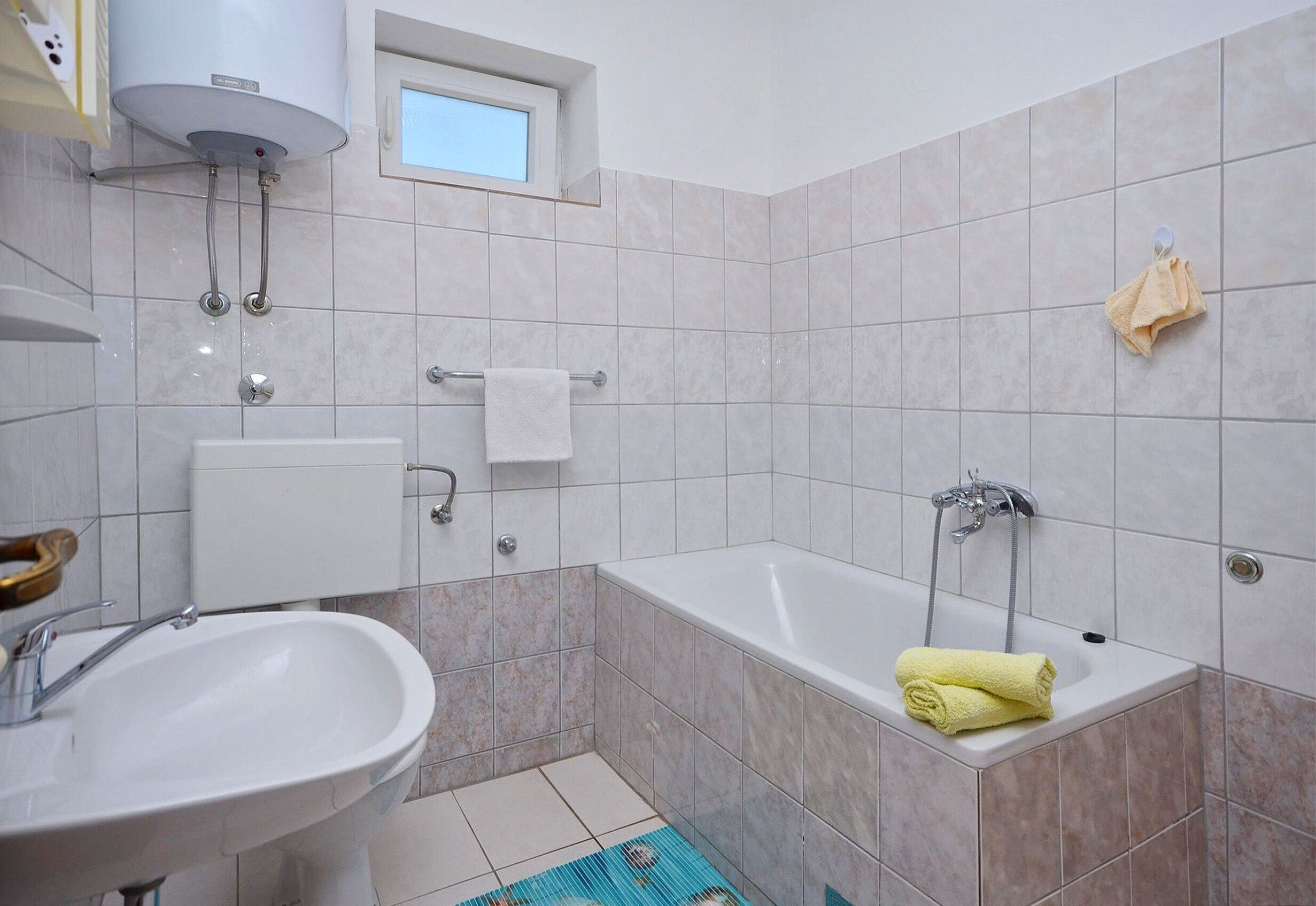 A bathroom with a bathtub, a sink, a window, and a towel rack.