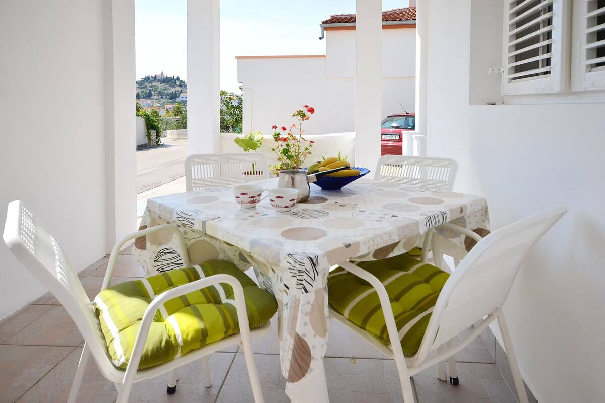 A round table with a white tablecloth and green cushions, surrounded by white chairs.