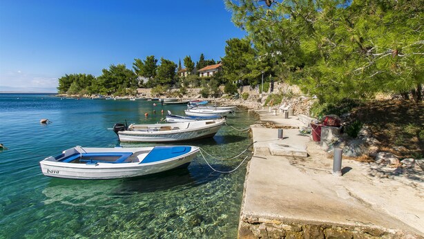 A coastal scene with clear water, boats moored at the shore, and buildings in the background. - Apartment Tina (Starigrad - Paklenica)