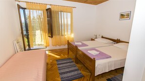 A bedroom with a bed, a bedside table, a window with curtains, and a wooden floor. - Apartment Tina (Starigrad - Paklenica)
