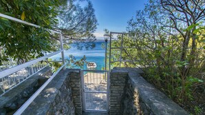 A stone staircase leading to a gate overlooking a body of water, surrounded by greenery. - Apartment Tina (Starigrad - Paklenica)