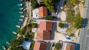 An aerial view of a coastal area with several buildings, a paved road, and multiple boats docked along the shore. - Apartment Tina (Starigrad - Paklenica)
