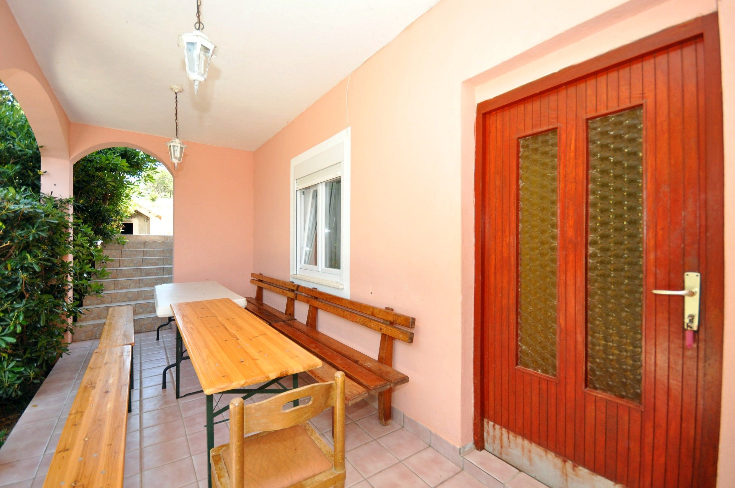A patio area with a wooden table and benches, a door with a window, and a staircase leading to an upper level.