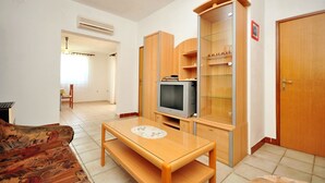 A living room with a sofa, a wooden table with a bench, a television, and built-in shelving. - Apartments Andelo (Vlasici)