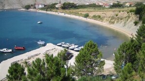 A coastal area with boats docked near the shore, a sandy beach, and buildings in the background. - Apartments Andelo (Vlasici)