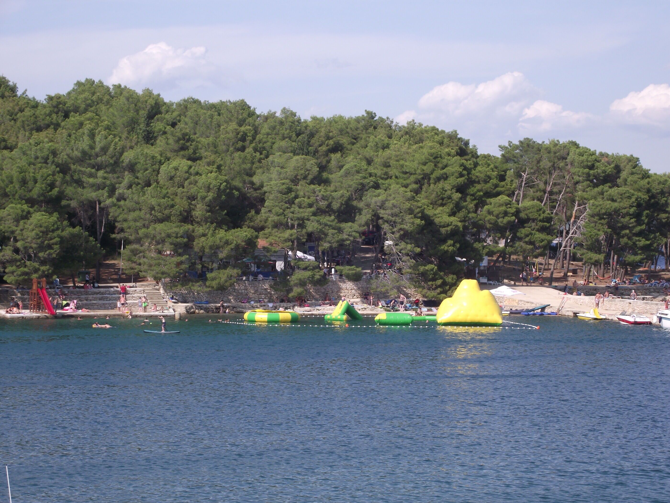 Une plage avec des jeux d’eau gonflables et un toboggan rouge.