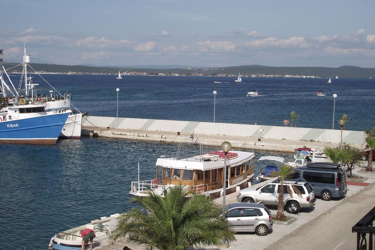 Un port de plaisance avec des bateaux amarrés, un petit service de location de bateaux et des voitures garées le long de la promenade.