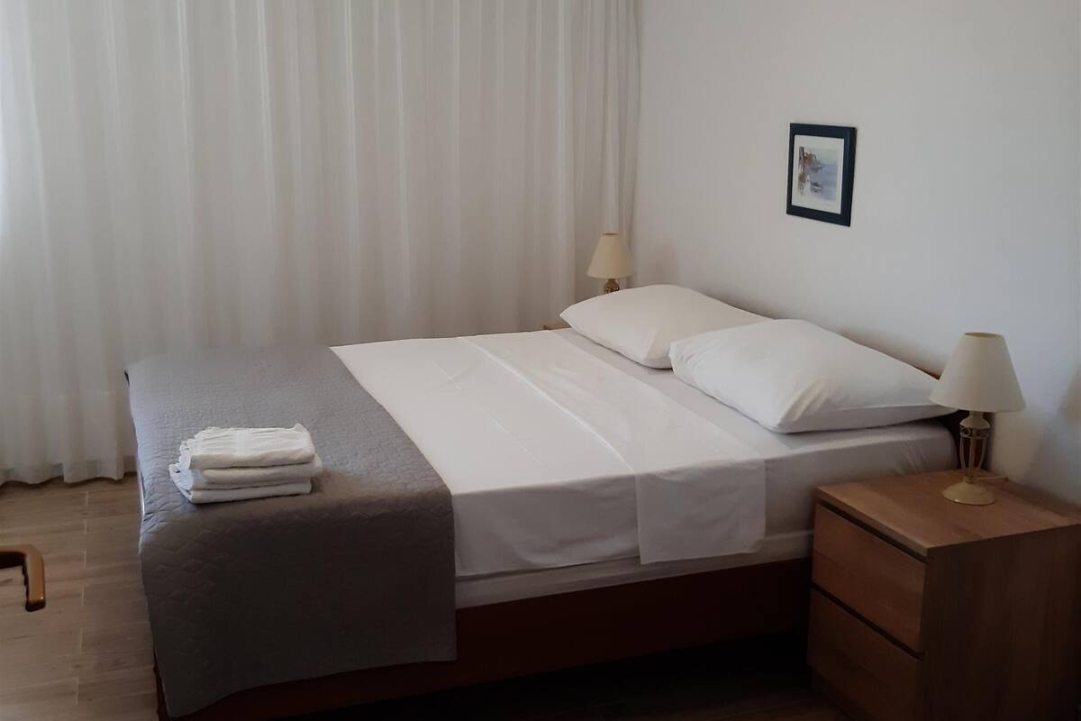 Un lit bien fait, avec du linge de lit blanc et une serviette pliée, une table de chevet avec une lampe et un plancher en bois.