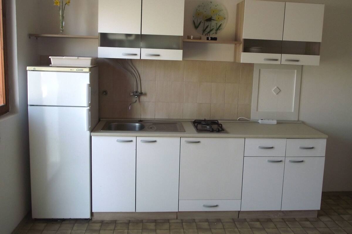 Une cuisine de taille réduite avec des meubles blancs, un évier encastré et une cuisinière.