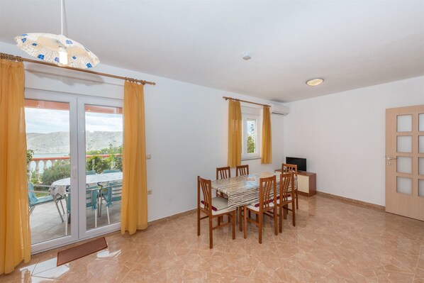 A dining area with a table and chairs, a television, and a view through a glass door. - Apartments Andelo II (Vlasici)