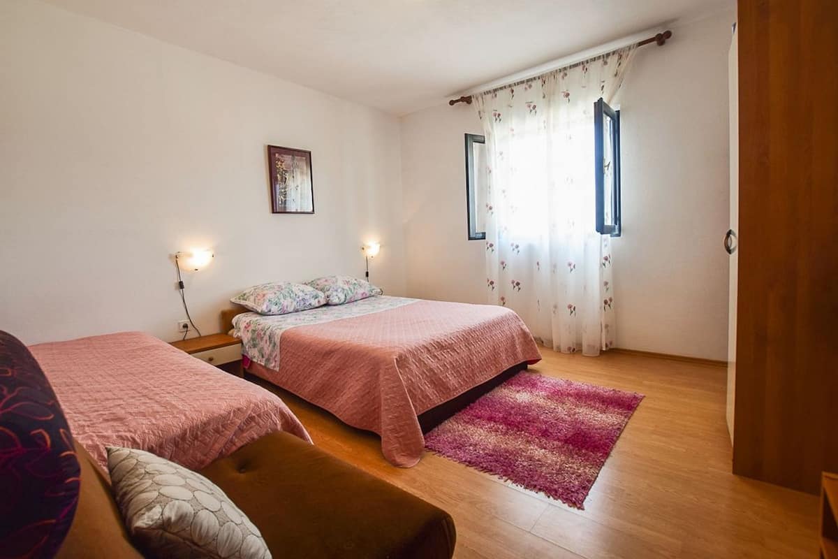 A bedroom with two beds, a wooden floor, a pink rug, and a window with floral curtains.