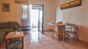 A living room with a sofa, a small table with a plant, a dining area with a table and chairs, and a sliding glass door leading to a balcony.