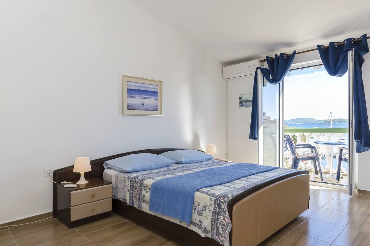 A bedroom with a bed, bedside tables, a lamp, a framed picture, and a balcony with a view.